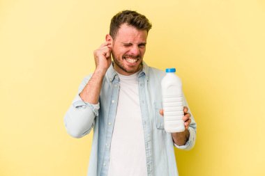 Beyaz bir adam elinde bir şişe süt tutuyor sarı arka planda izole edilmiş kulakları elleriyle kapatıyor..