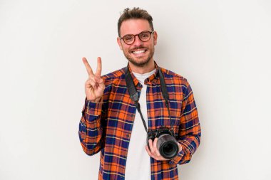 Beyaz arka planda izole edilmiş beyaz fotografçı neşeli ve tasasız parmakları olan bir barış sembolü gösteriyor..