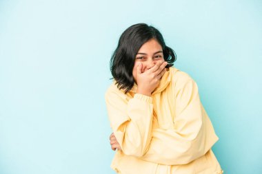 Genç Latin bir kadın mavi arka planda izole edilmiş gülerek, kaygısız, doğal duygular içinde..