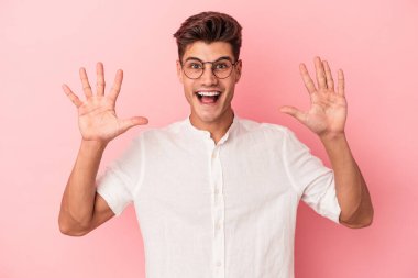 Pembe arka planda izole edilmiş genç beyaz adam hoş bir sürpriz alıyor, heyecanlı ve el kaldırıyor..