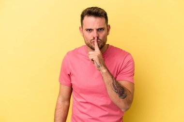 Sarı arka planda izole edilmiş genç beyaz bir adam ya sır saklıyor ya da sessizlik istiyor..