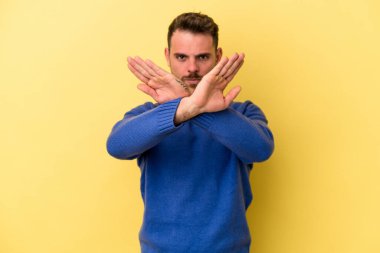 Sarı arka planda izole edilmiş genç beyaz adam inkar jesti yapıyor.