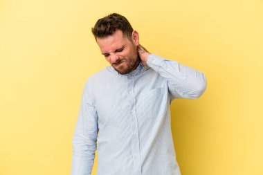 Sarı arka planda izole edilmiş genç beyaz bir adam stresten dolayı boynu ağrıyor, masaj yapıyor ve elle dokunuyor..