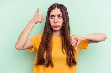 Yeşil arka planda izole edilmiş genç beyaz kadın baş parmağını kaldırıyor, zor seçim konsepti.