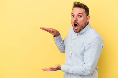 Sarı arka planda izole edilmiş genç beyaz adam elleri arasında bir kopya alanı tutarken şok ve hayrete düştü..