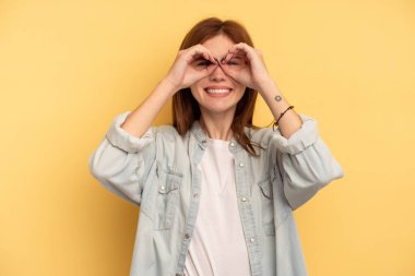 Sarı arka planda izole edilmiş genç bir İngiliz kadın. Gözlerinde işaret var.