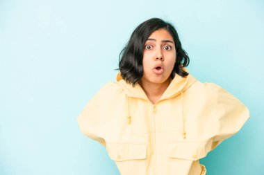 Mavi arka planda izole edilmiş genç Latin kadın gördüğü bir şey yüzünden şoka uğruyor..
