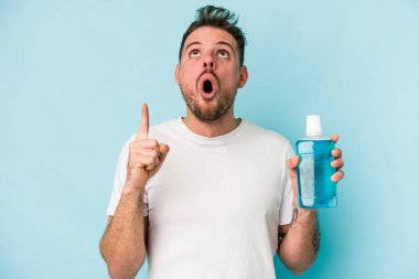 Elinde gargara tutan beyaz bir adam mavi arka planda izole edilmiş, ağzı açık, üst tarafı işaret ediyor..