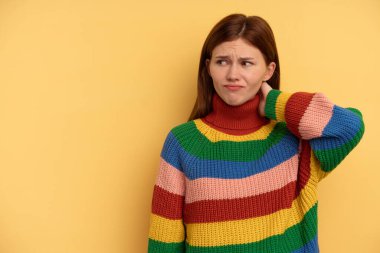 Sarı arka planda izole edilmiş genç bir İngiliz kadın kafasının arkasına dokunuyor, düşünüyor ve bir seçim yapıyor..