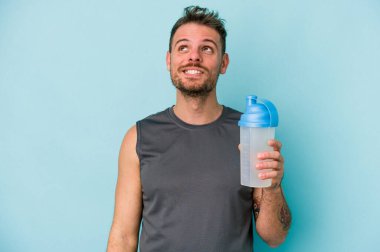 Kafkasyalı genç adam milkshake içiyor mavi arka planda izole edilmiş hedeflere ve amaçlara ulaşmayı hayal ediyor.