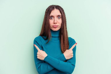 Yeşil arka plan noktalarında izole edilmiş genç beyaz kadın, iki seçenek arasında seçim yapmaya çalışıyor..