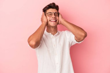 Pembe arka planda izole edilmiş genç beyaz adam ellerini başının üstünde tutarak neşeyle gülüyor. Mutluluk kavramı.