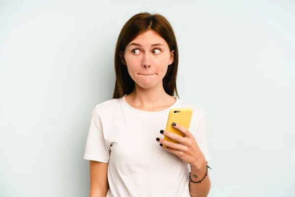 Ung Engelsk Kvinna Som Håller Mobiltelefon Isolerad Blå Bakgrund Förvirrad — Stockfoto