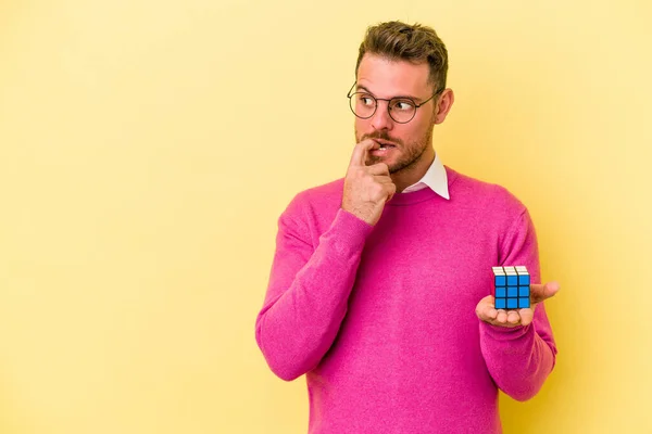 Mladý Běloch Drží Rubiksovu Kostku Izolovanou Žlutém Pozadí Uvolněně Přemýšlející — Stock fotografie