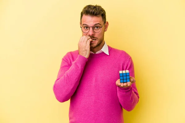 Mladý Běloch Drží Rubiks Kostku Izolované Žlutém Pozadí Kousání Nehty — Stock fotografie