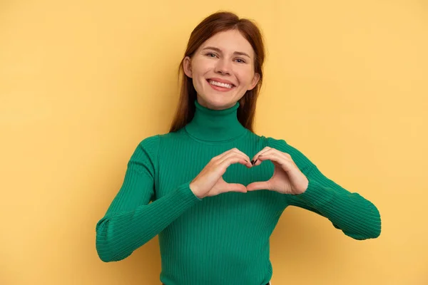 Stock image Young English woman isolated on yellow background smiling and showing a heart shape with hands.