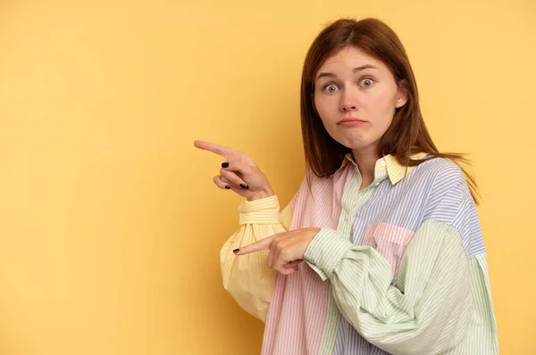 Young English woman isolated on yellow background shocked pointing with index fingers to a copy space.