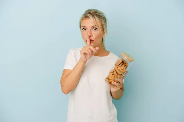 Young Russian Woman Holding Cookies Isolated Blue Background Keeping Secret — Stock Photo, Image