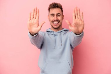 Pembe arka planda izole edilmiş genç beyaz adam on numarayı elleriyle gösteriyor..