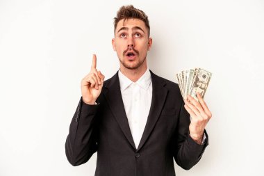 Kafkasyalı genç bir iş adamı elinde banknotlar tutarken beyaz arka planda, ağzı açık bir şekilde üst tarafı işaret ediyor..