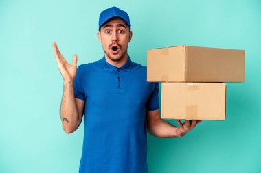 Genç teslimatçı beyaz adam mavi arka planda izole edildi. Şaşırdı ve şok oldu..