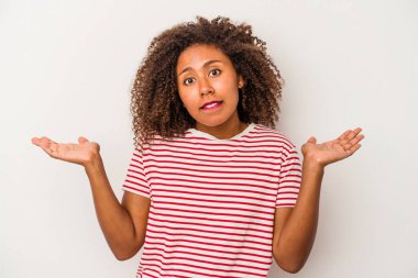 Beyaz arka planda yalıtılmış kıvırcık saçlı, genç Afrikalı Amerikalı kadın. Kopya alanını tutmak için omuz silkme konusunda kafası karışık ve kuşkulu..