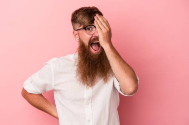 Pembe arka planda uzun sakallı beyaz bir adam yüzünün yarısını avuç içiyle örterek eğleniyor..