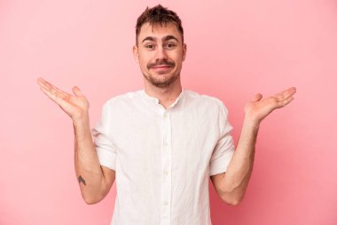 Pembe arka planda soyutlanmış genç beyaz bir adam sorgulama sırasında omuz silkiyor ve şüphe duyuyor..