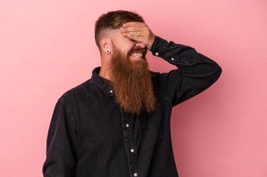 Pembe arka planda, uzun sakallı, beyaz, genç bir adam. Gözleri ellerle kaplıyor. Gülümsüyor ve bir sürpriz bekliyor..