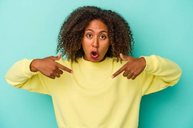 Kıvırcık saçlı genç Afro-Amerikalı kadın, mavi arka planda izole edilmiş, parmakları aşağıda, olumlu hisler içinde..