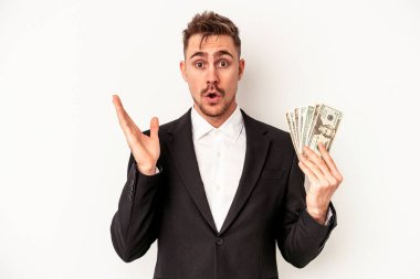 Kafkasyalı genç iş adamı elinde banknotlar tutarken beyaz arka planda izole edilmiş, şaşırmış ve şok olmuş..