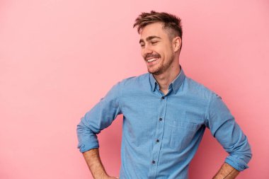 Pembe arka planda izole edilmiş genç beyaz adam mutlu bir şekilde gülüyor ve ellerini karnının üstünde tutarak eğleniyor..