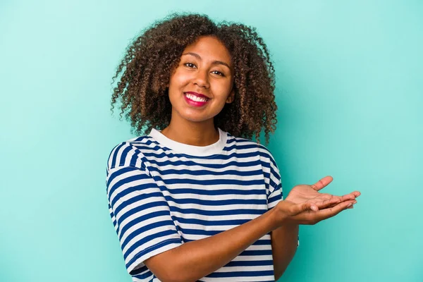 stock image Young african american woman with curly hair isolated on blue background holding a copy space on a palm.