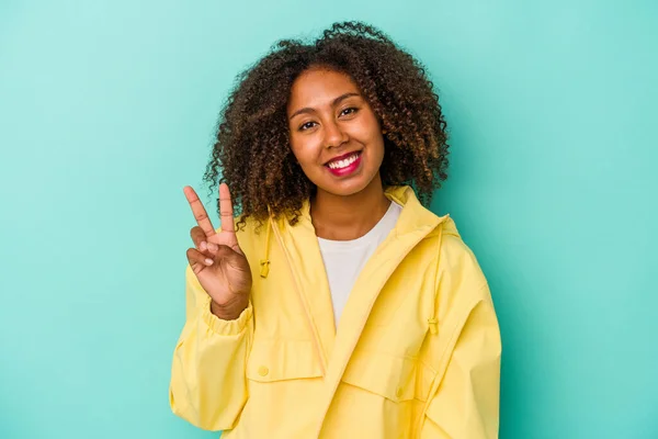 若いアフリカ系アメリカ人の女性は 青の背景に喜びと屈託のない指で平和のシンボルを示して隔離された巻き毛 — ストック写真