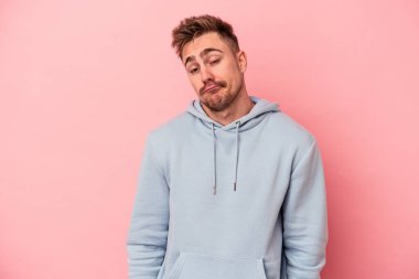 Pembe arka planda izole edilmiş genç beyaz adam omuzlarını silkeliyor ve gözleri açık..