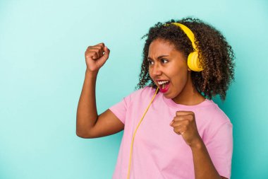 Mavi arka planda izole edilmiş müzik dinleyen genç Afrikalı Amerikalı kadın zaferden sonra yumruğunu kaldırıyor, kazanan konsept.