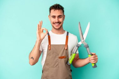 Genç bahçıvan elinde makas tutan beyaz adam mavi arka planda izole edilmiş neşeli ve kendinden emin..