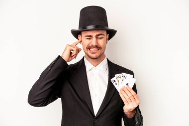 Beyaz arka planda izole edilmiş, elleri kulaklarında sihirli bir kart tutan Kafkasyalı genç büyücü..