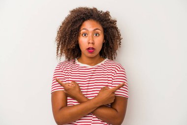 Beyaz arka planda yalıtılmış kıvırcık saçlı Afrikalı Amerikalı genç bir kadın iki seçenek arasında seçim yapmaya çalışıyor..