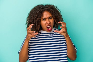 Mavi arka planda izole edilmiş kıvırcık saçlı genç Afro-Amerikalı kadın öfkeyle bağırıyor..