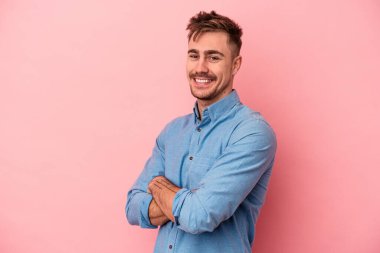 Pembe arka planda izole edilmiş genç beyaz adam kendini güvende hissediyor, kararlılıkla kollarını kavuşturuyor..