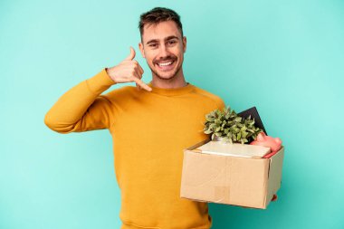 Genç beyaz adam mavi arka planda izole edilmiş bir şekilde hareket ediyor. Parmakları olan bir cep telefonu hareketi gösteriyor..