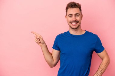 Pembe arka planda izole edilmiş genç beyaz adam işaret parmağıyla işaret ederek gülümsüyor..