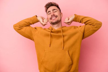 Pembe arka planda izole edilmiş genç beyaz adam kollarını uzatıyor, rahat bir konumda..