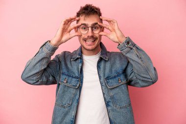 Pembe arka planda izole edilmiş genç beyaz adam bir başarı fırsatı bulmak için gözlerini açık tutuyor..