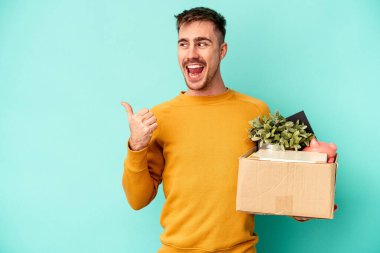 Kafkasyalı genç bir adam mavi arka plan noktalarında izole bir hareket yapıyor başparmak uzakta, gülüyor ve kaygısız.