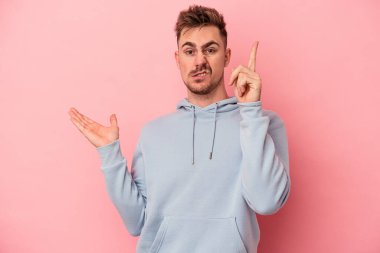 Pembe arka planda izole edilmiş genç beyaz adam elinde bir ürün tutuyor..