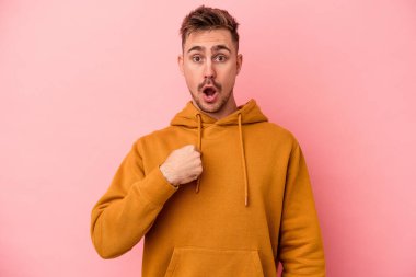Pembe arka planda izole edilmiş genç beyaz adam parmağını göstererek şaşırdı, geniş bir gülümsemeyle..