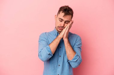 Pembe arka planda izole edilmiş genç beyaz adam esniyor. Ağzı eliyle kapatan yorgun bir hareket sergiliyor..