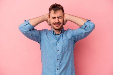 Pembe arka planda izole edilmiş genç beyaz adam kulaklarını elleriyle kapatıyor..